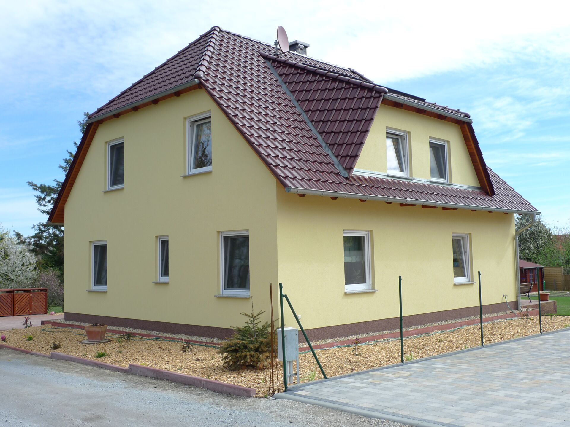 Gelbes Einfamilienhaus mit braunen Dachziegeln und gepflasterter Zufahrt, erbaut von Weier Bau.